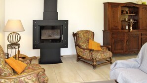 A living room with a black wood-burning stove, two floral-patterned armchairs, a wooden cabinet, and a table.
