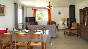 A dining area with a table set for four, surrounded by wooden chairs. A sofa is positioned against the wall, and a television is mounted above it.
