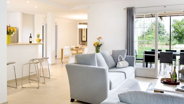 Una sala de estar moderna con un sofá gris, un comedor y una cocina a la vista.