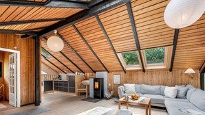Een ruime loft met hoge plafonds, houten balken, een gezellige zithoek met een bank en een kleine tafel, een keukenhoek en een groot dakraam.