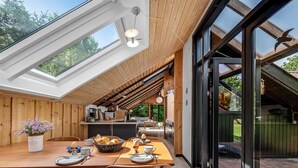 Een moderne keuken met houten details, een eethoek met een houten tafel en stoelen, en grote ramen voor veel daglicht.