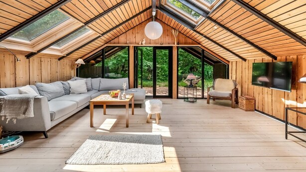 Een ruime loft met houten vloeren, een grijze bank, een salontafel en een aan de muur bevestigde televisie.