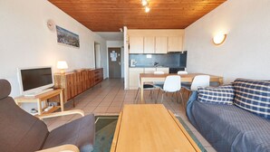 Un espace de vie compact doté d’un plafond en bois, d’un téléviseur, d’un canapé, d’une table à manger et d’un coin cuisine.
