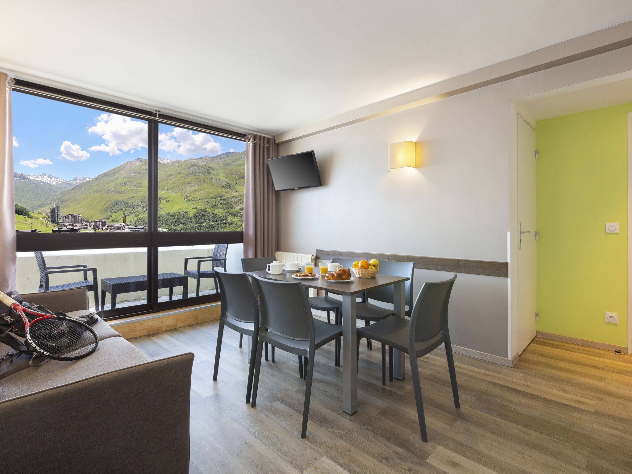 A dining area with a table set for two, a tennis racket, and a view of mountains through large windows.