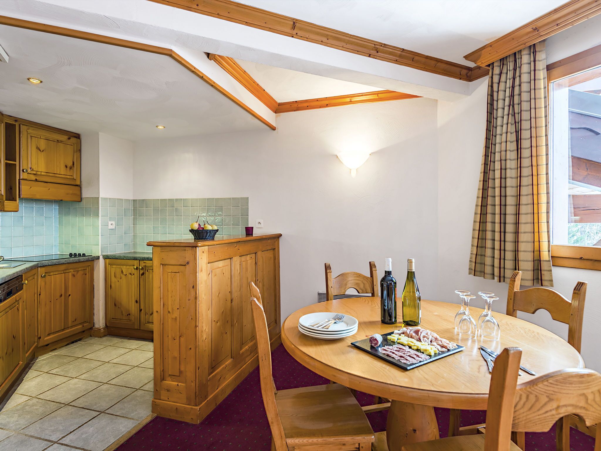 A kitchen with wooden cabinets, a tiled backsplash, and a dining area with a round table set for four.