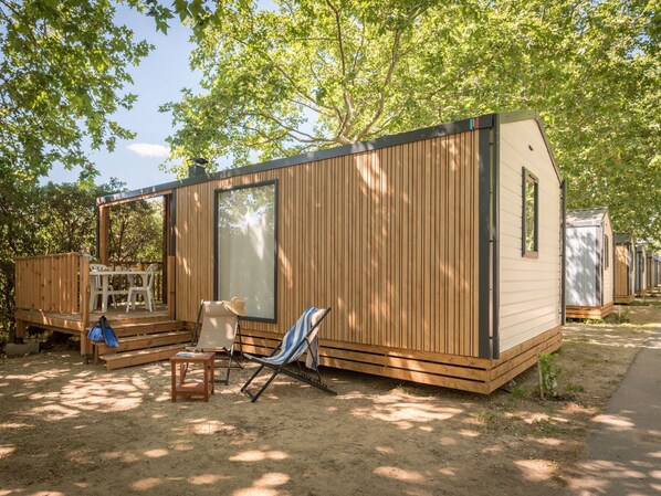 A wooden mobile home with a deck, a dining area, and a lounge chair.