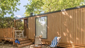 Une cabane en bois dotée d’une terrasse, d’un espace salon couvert et d’une grande fenêtre.