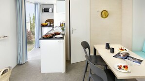 A compact kitchen with a microwave, sink, and dining area with a table and chairs. - Camping La Plage by Interhome (Argelès sur Mer)