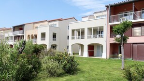 A row of multi-story buildings with balconies, a well-maintained lawn, and a clear sky. - Catalana by Interhome (Le Barcarès)