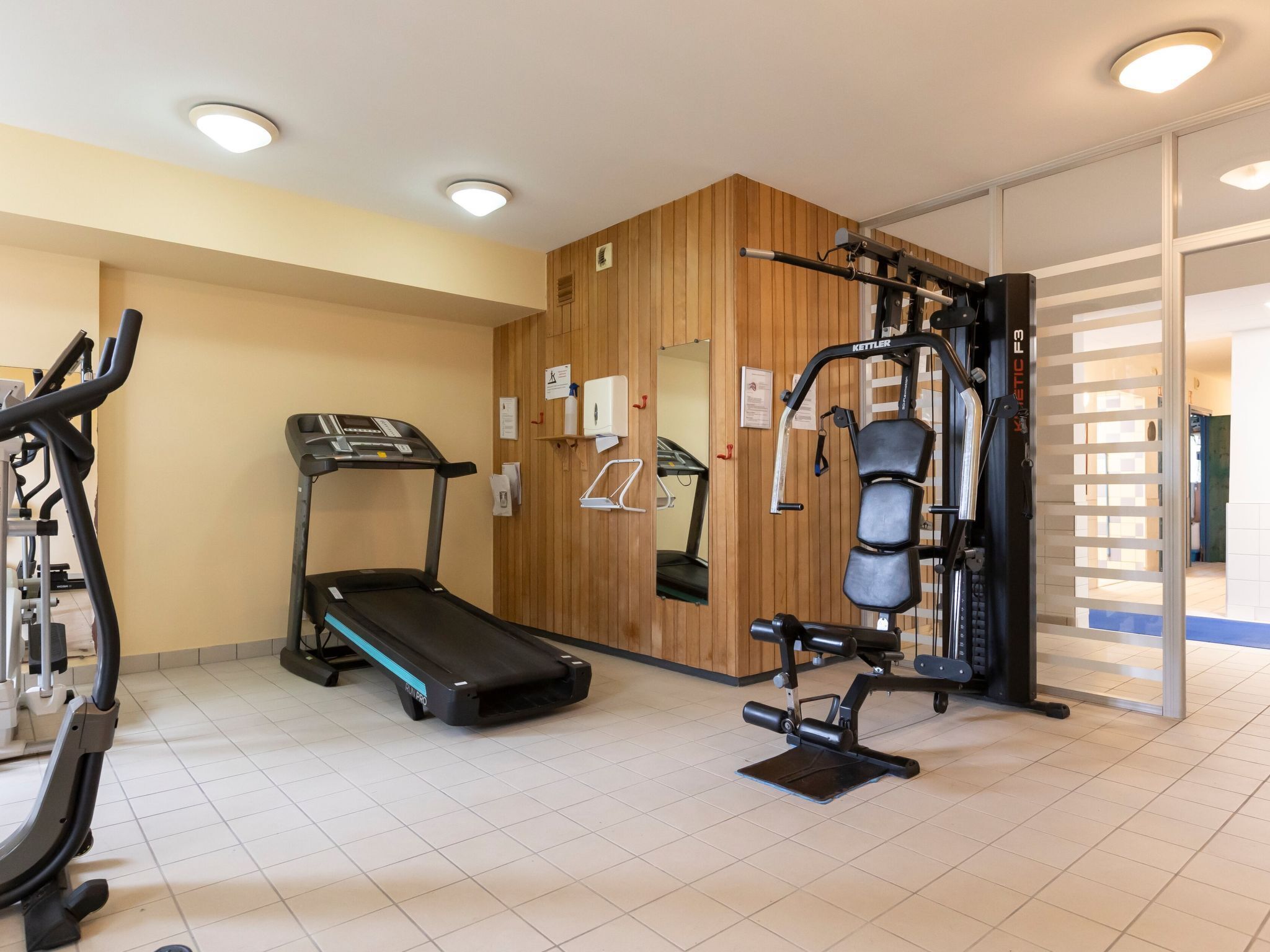 A gym with a treadmill, weight machines, and a mirrored wall.