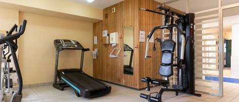 A gym with a treadmill, weight machines, and a mirrored wall.