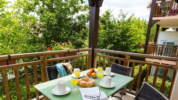 A balcony with a table set for breakfast, including croissants, fruit, and drinks. - Odalys Référence Le Domaine des Rois by Interhome (Bergheim)