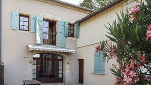 Un bâtiment à deux étages doté d’un balcon, d’un banc en bois et d’un pot de fleurs contenant des fleurs roses.