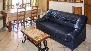 Un salon avec un canapé en cuir, une table à manger avec des chaises, et un coin cuisine à l’arrière-plan.