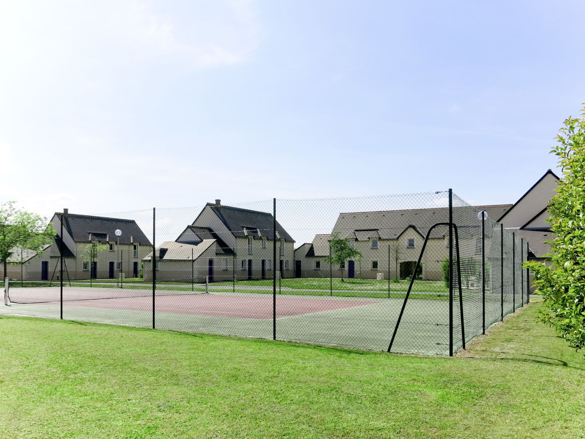 Un quartier résidentiel avec des maisons, un terrain de sport délimité par une clôture et un champ d’herbe.