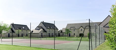 Zona residencial com casas, quadra esportiva cercada e um campo gramado.