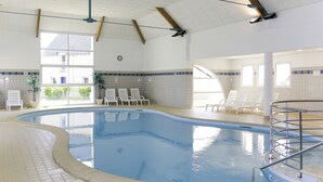 Piscina interior com água cristalina, rodeada por espreguiçadeiras e piso em mosaico.