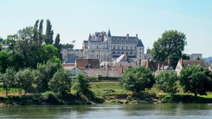 A historic building with a prominent tower, surrounded by trees and a river.