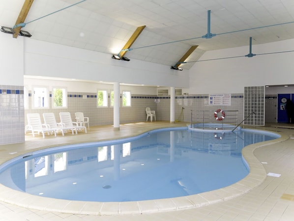 An indoor swimming pool with a tiled floor, a lifebuoy, and a sign indicating the pool area.