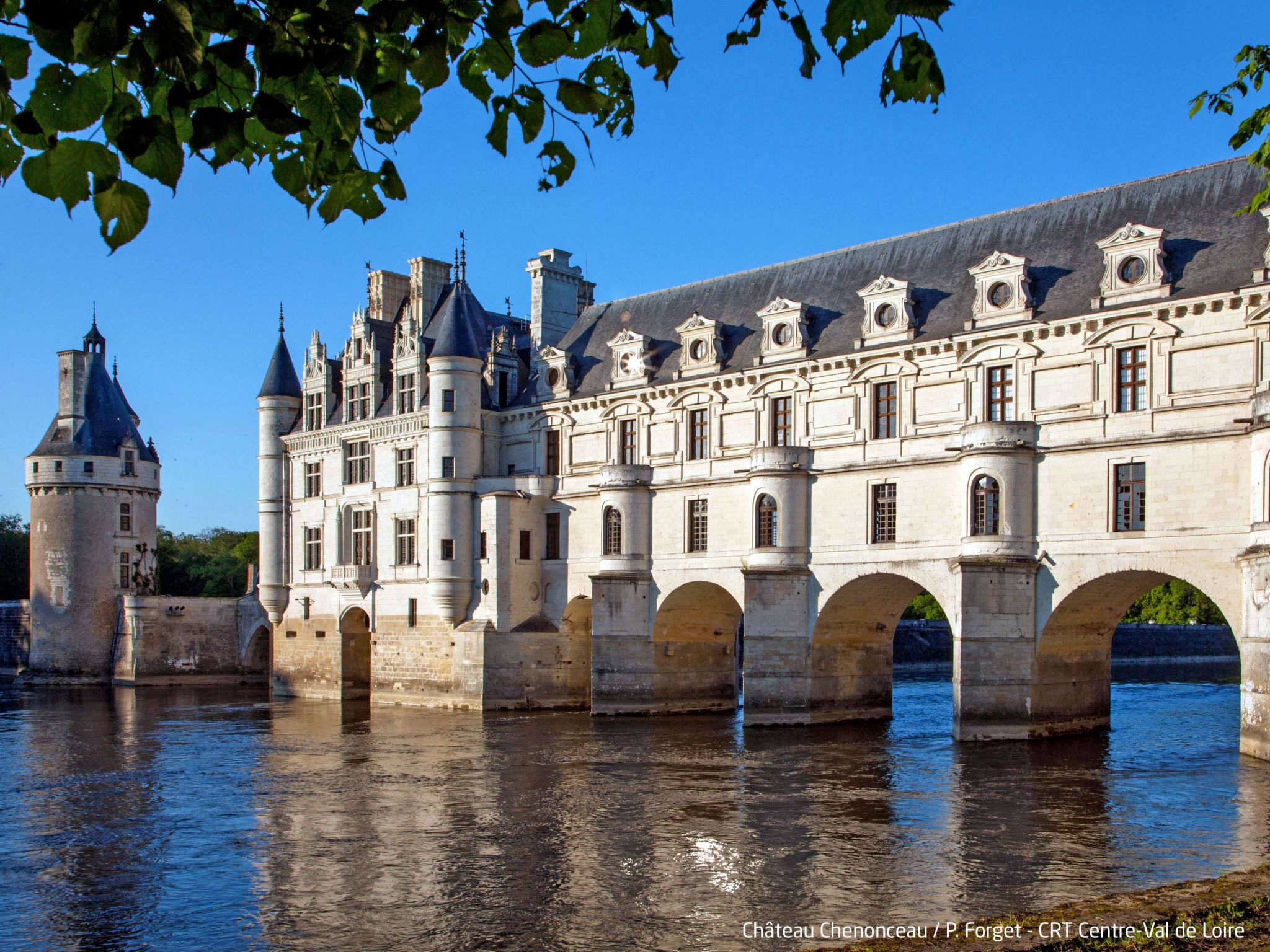 Château Chenonceau, a historic château with a bridge over the river, featuring classical architecture and a prominent tower.