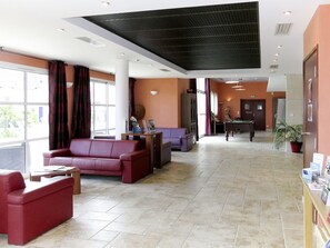 Un hall con un sofá rojo, mesa de billar y mostrador de recepción.