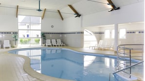An indoor swimming pool with clear water, surrounded by lounge chairs and a tiled floor.