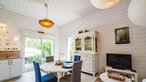 Eine moderne Küche mit weißen Schränken, ein Essbereich mit blauen Stühlen, ein Schrank mit Glastüren, ein Fernseher und ein farbenfroher Teppich.