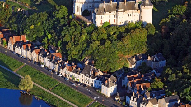 Eine Vogelperspektive auf eine historische Burg, umgeben von einer Stadt mit engen Gassen und einem Fluss.