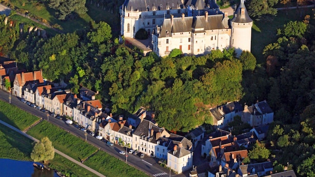 An aerial view of a historic castle surrounded by a town with narrow streets and a river.