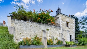 A stone building with a balcony, surrounded by lush greenery and flowering plants.