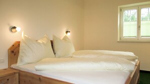 Una cama de madera con ropa de cama blanca, dos mesitas de noche y luces fijadas a la pared.