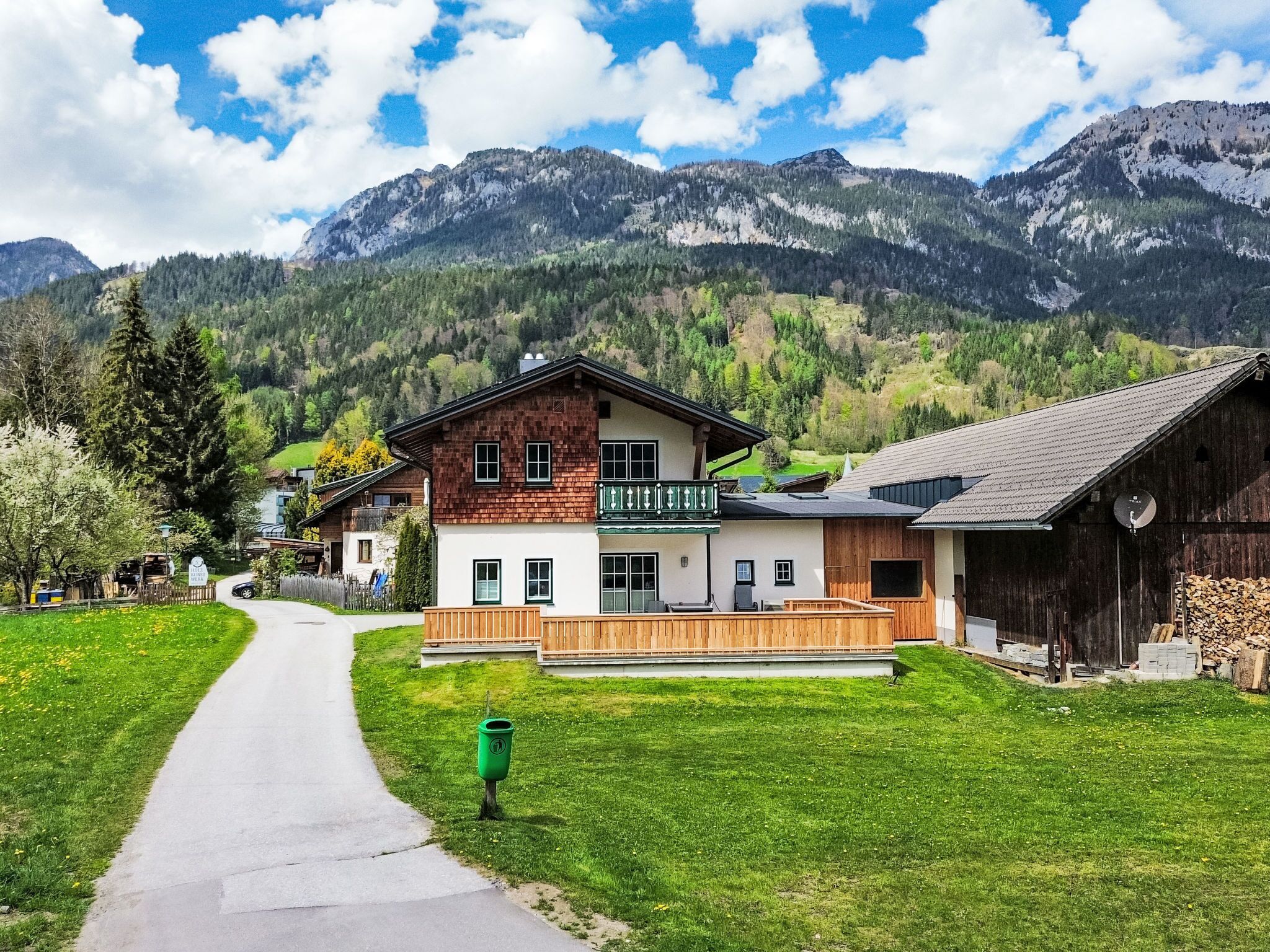 Un bâtiment à deux étages doté d’un balcon, entouré d’une végétation luxuriante et avec des montagnes en arrière-plan.