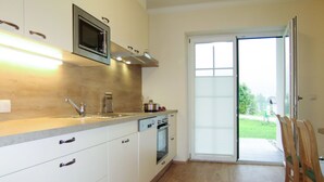 Cocina moderna equipada con microondas, estufa y lavavajillas. Posee una puerta corrediza de vidrio que da a un patio con mobiliario exterior.