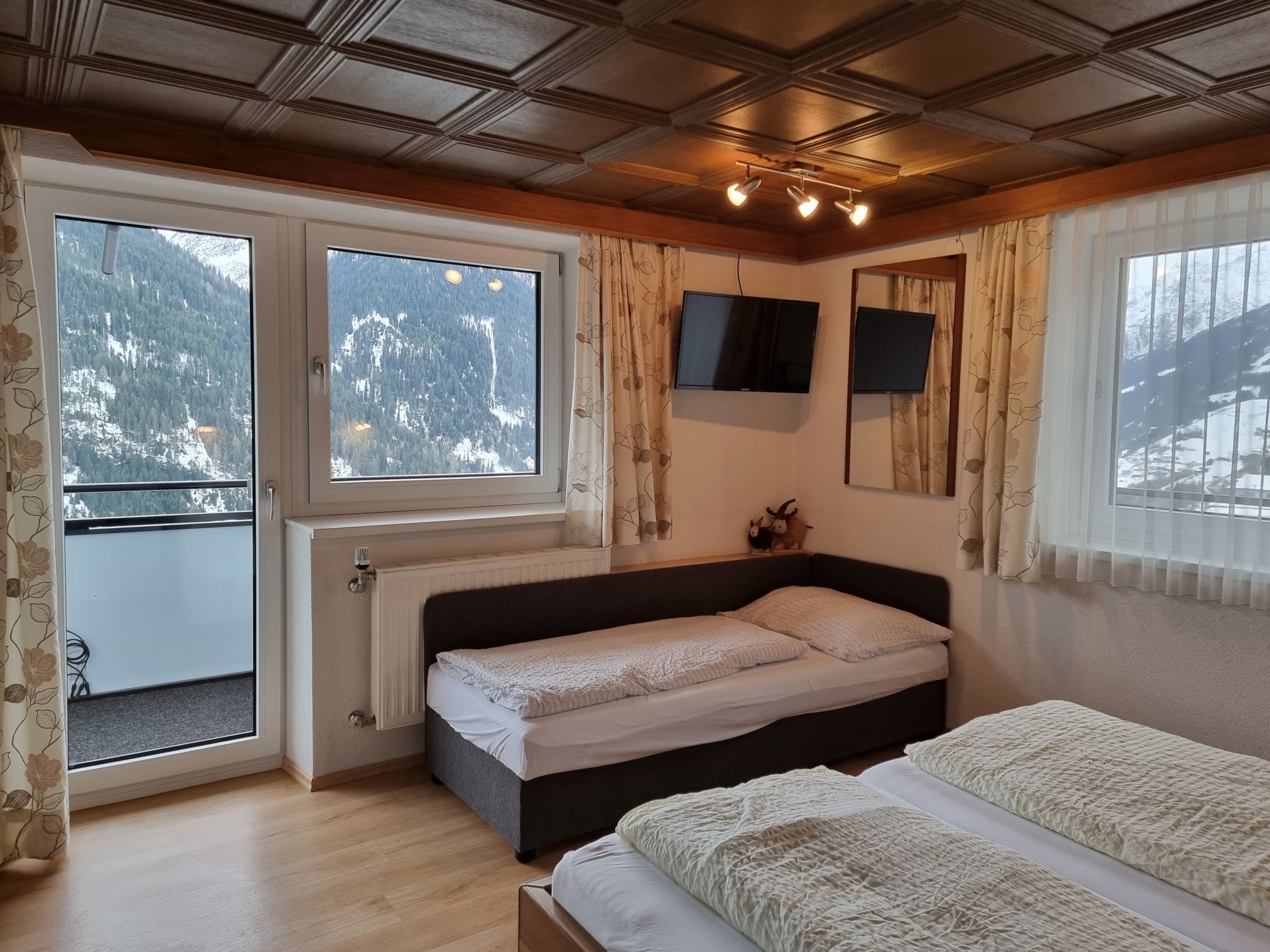 Une chambre avec deux lits, une fenêtre donnant sur des montagnes enneigées, un radiateur et un téléviseur fixé au mur.