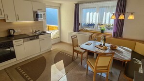 Une cuisine moderne avec des meubles blancs, une cuisinière et un four à micro-ondes. On y trouve un coin repas avec une table et des chaises, ainsi qu’une fenêtre avec des rideaux.