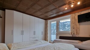 Une chambre avec deux lits, une armoire, une fenêtre donnant sur des montagnes enneigées et un téléviseur fixé au mur.