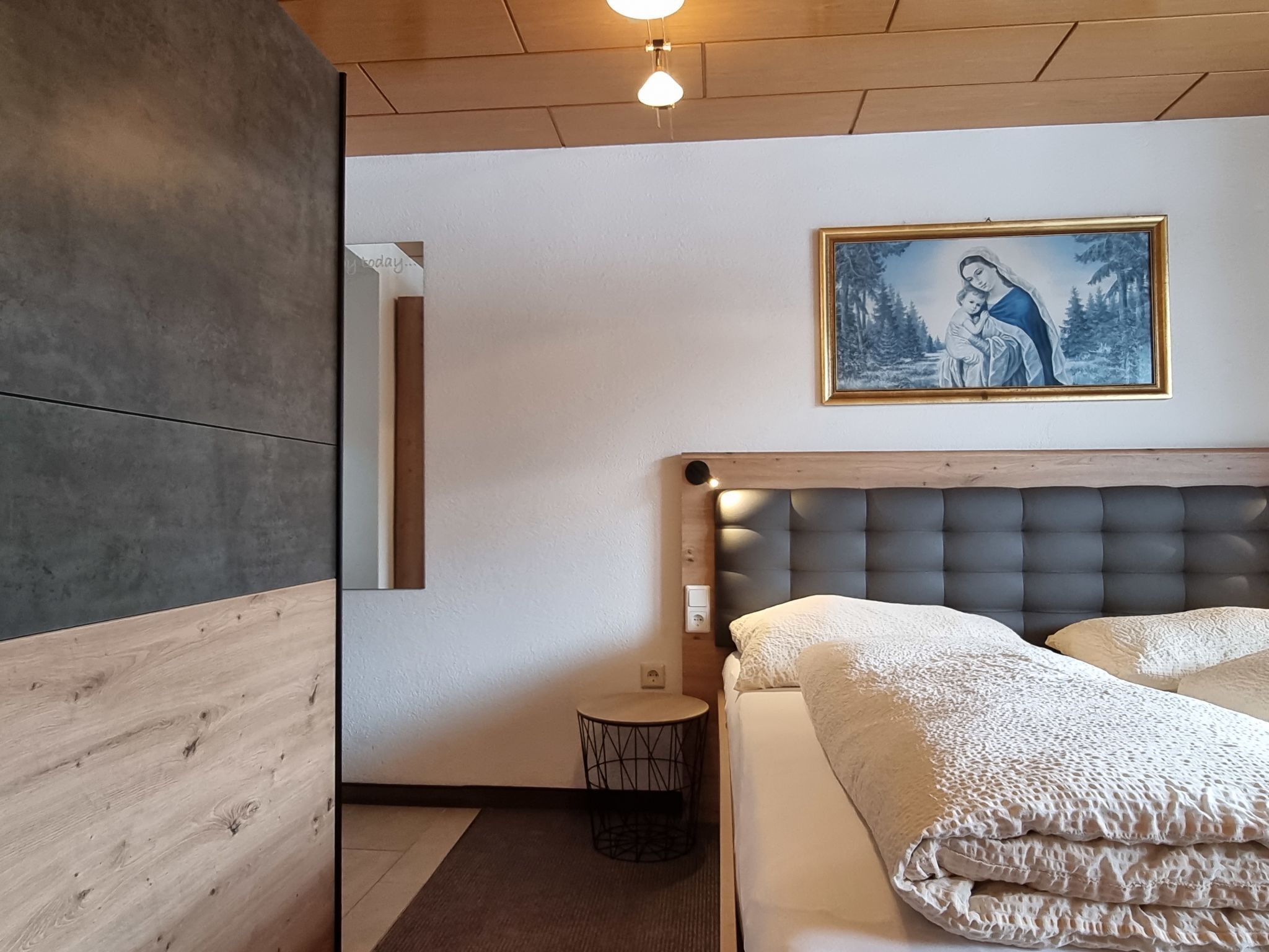A modern bedroom with a large bed, a small round table, and a painting on the wall.