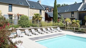 A pool area with lounge chairs and a stone building in the background. - Les Hauts de la Houle 24 by Interhome (Cancale)