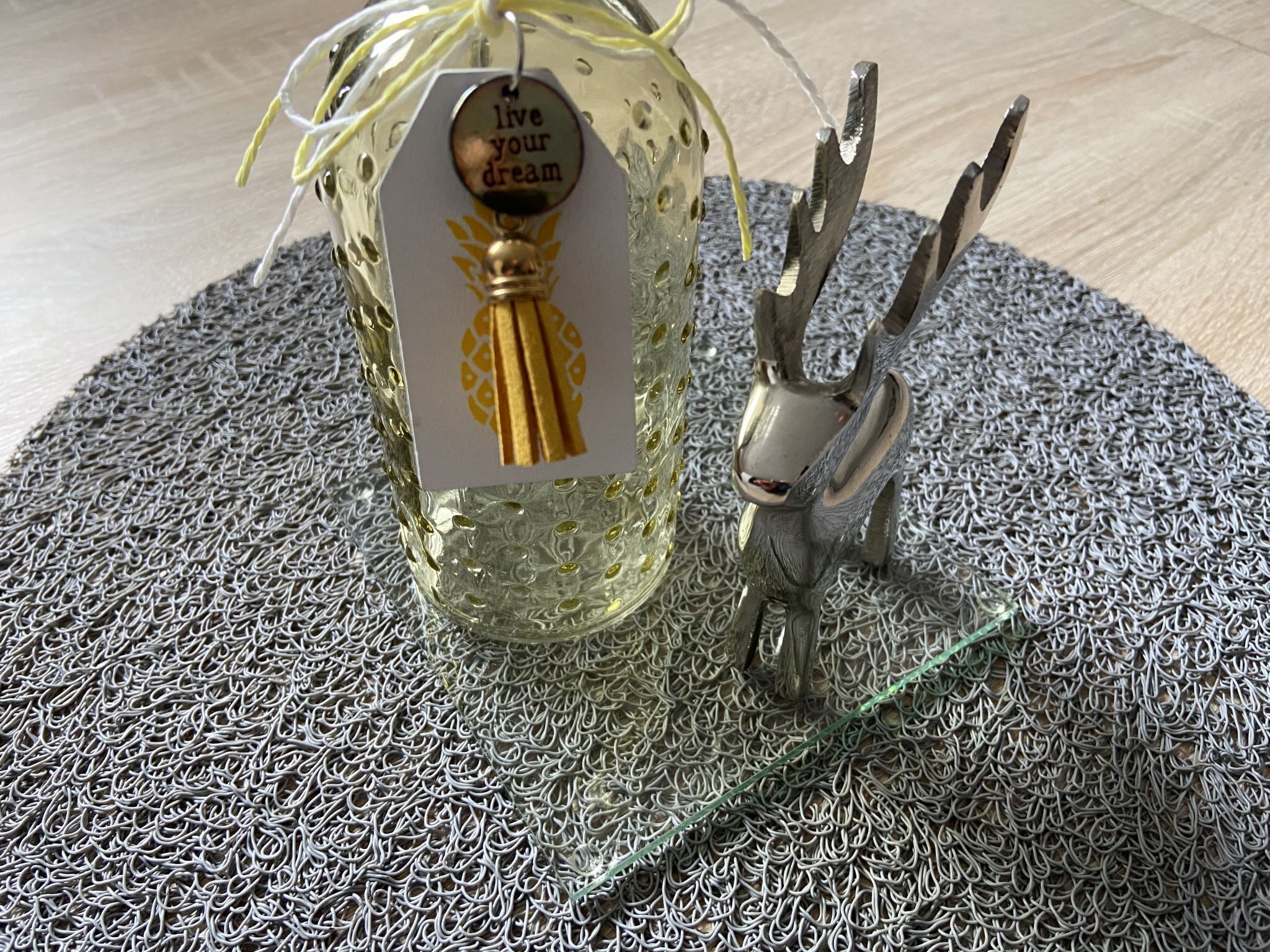 Een decoratieve glazen fles met een label waarop staat 'live your dream' en een metalen beeldje van een konijn op een gestructureerd oppervlak.