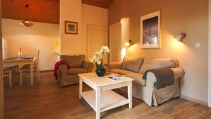 Ein Wohnzimmer mit Holzbalkendecke, einem Essbereich mit Tisch und Stühlen sowie einem Sofa mit Blumenvase.