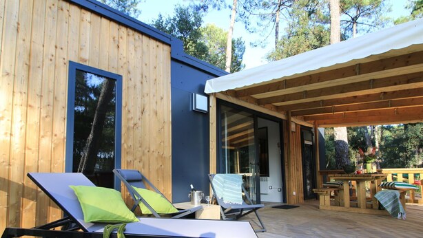 A wooden deck with two sun loungers and a table, a covered area, and a building with large windows.