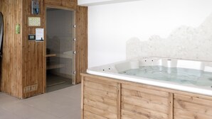 A wooden sauna room with a glass-enclosed hot tub, a sauna control panel, and a door leading to another room. - Les Balcons de l’Océan by Interhome (Biscarrosse)
