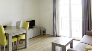 A modern living room with a dining area, a sofa, a TV, and a sliding glass door to the outside. - Les Balcons de l’Océan by Interhome (Biscarrosse)
