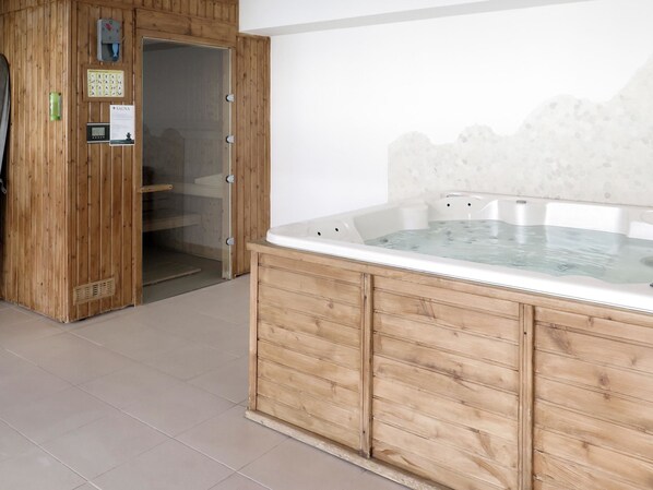 A wooden sauna room with a glass-enclosed hot tub, a sauna control panel, and a door leading to another room.
