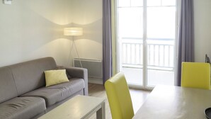 Een moderne woonkamer met een grijze bank, een klein tafeltje, gele stoelen en een vloerlamp.