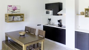 Una cocina moderna con armarios negros, encimera blanca y microondas. Hay una mesa de comedor de madera con sillas y una cesta. Un cuadro de flores cuelga en la pared sobre la cocina.
