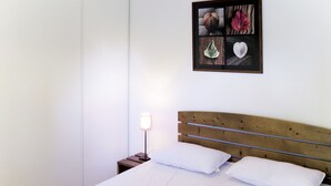 Una cama bien tendida con sábanas blancas y dos almohadas, un cabecero de madera, una lámpara de noche y un cuadro en la pared.