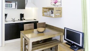 A compact kitchen with a microwave, stove, and sink. There is a wooden dining table with chairs and a TV on a wooden stand. - Les Terrasses du Lac by Interhome (Mimizan)