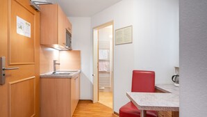 A compact kitchen with wooden cabinets, a sink, and a small dining area with a red chair and table. - Apartment Rosa by Interhome (Mayrhofen)