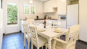 Una cocina moderna con armarios blancos, una mesa de comedor preparada para cuatro personas y un ventanal con vistas a zonas verdes.